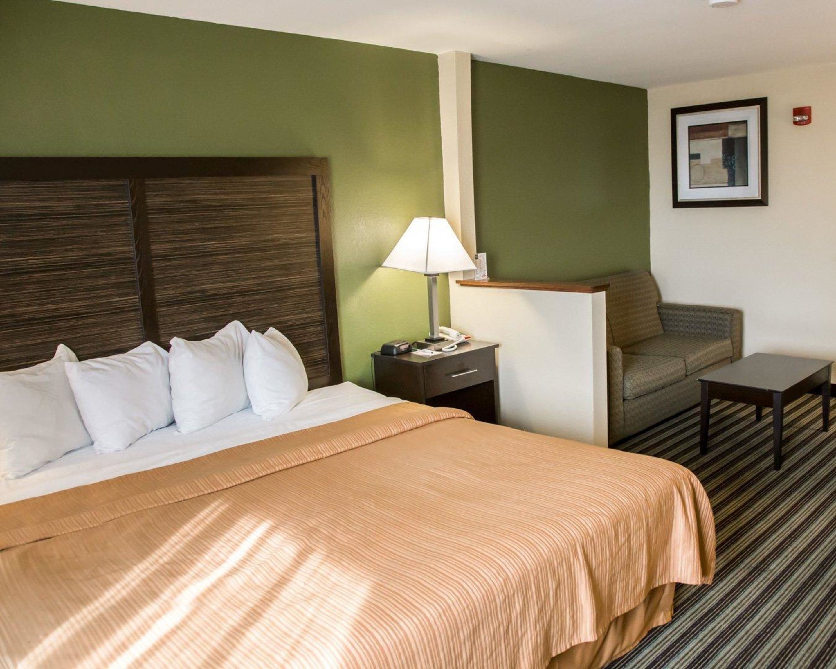 A hotel room with a large bed, a nightstand with a lamp, a sofa, and a small table.