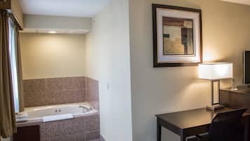 Une salle de bain d’hôtel avec une baignoire, un bureau avec une chaise, un tableau encadré au mur et une lampe.