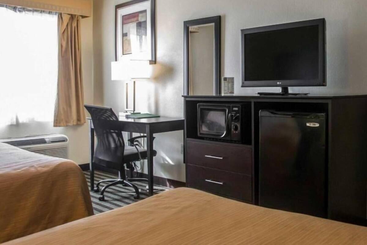 A hotel room with two beds, a desk with a chair, a television, a microwave, and a refrigerator.