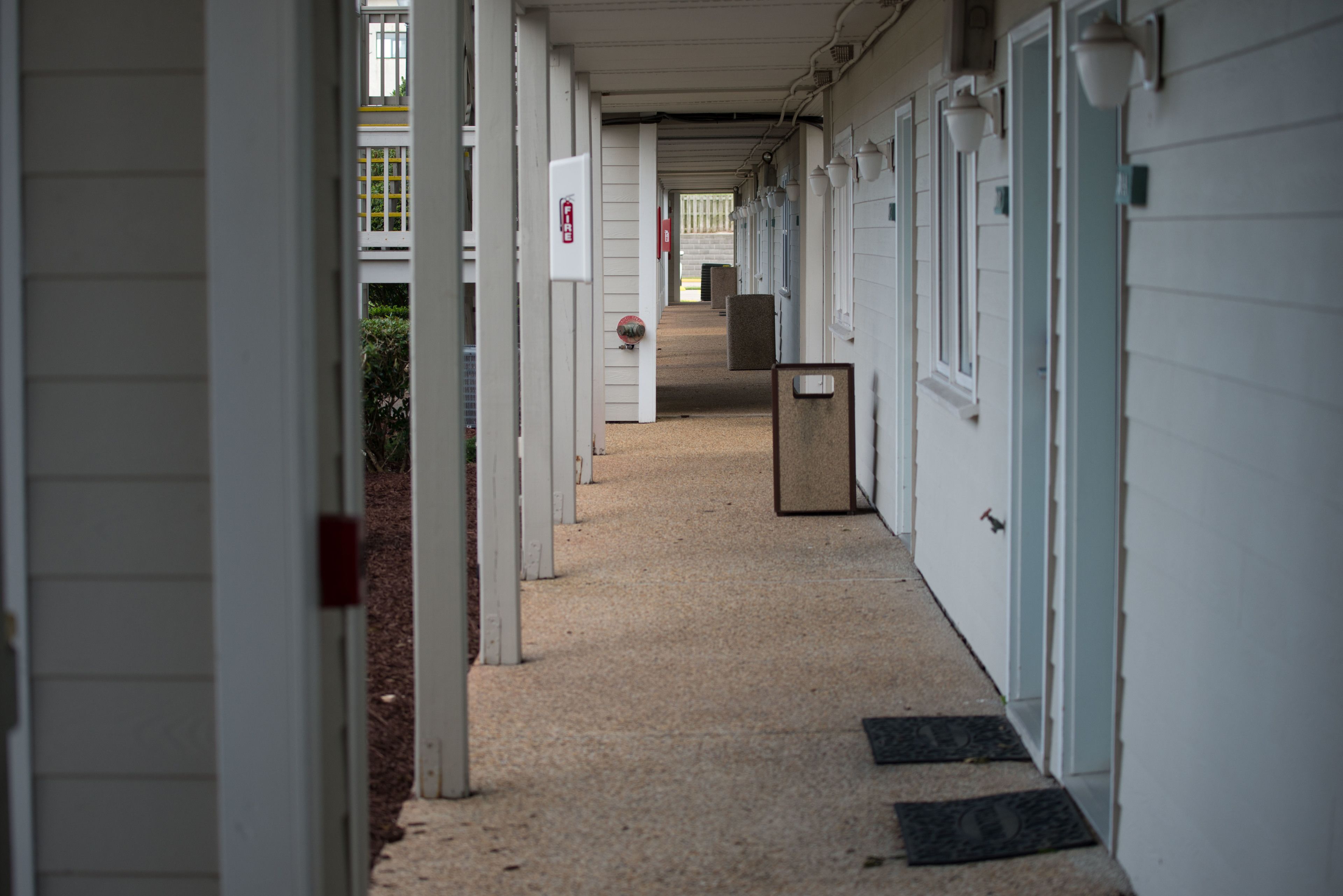 A corridor with white doors, a fire alarm, and a trash bin.