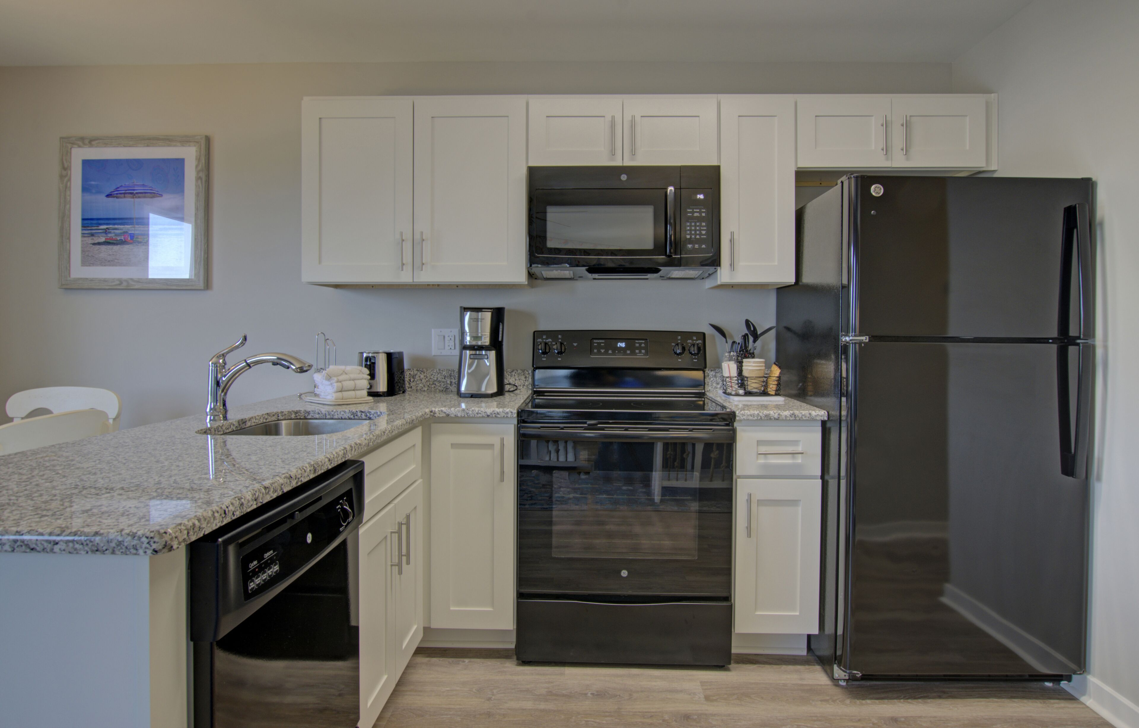 A modern kitchen with white cabinets, a stainless steel refrigerator, a microwave, an oven, and a dishwasher.