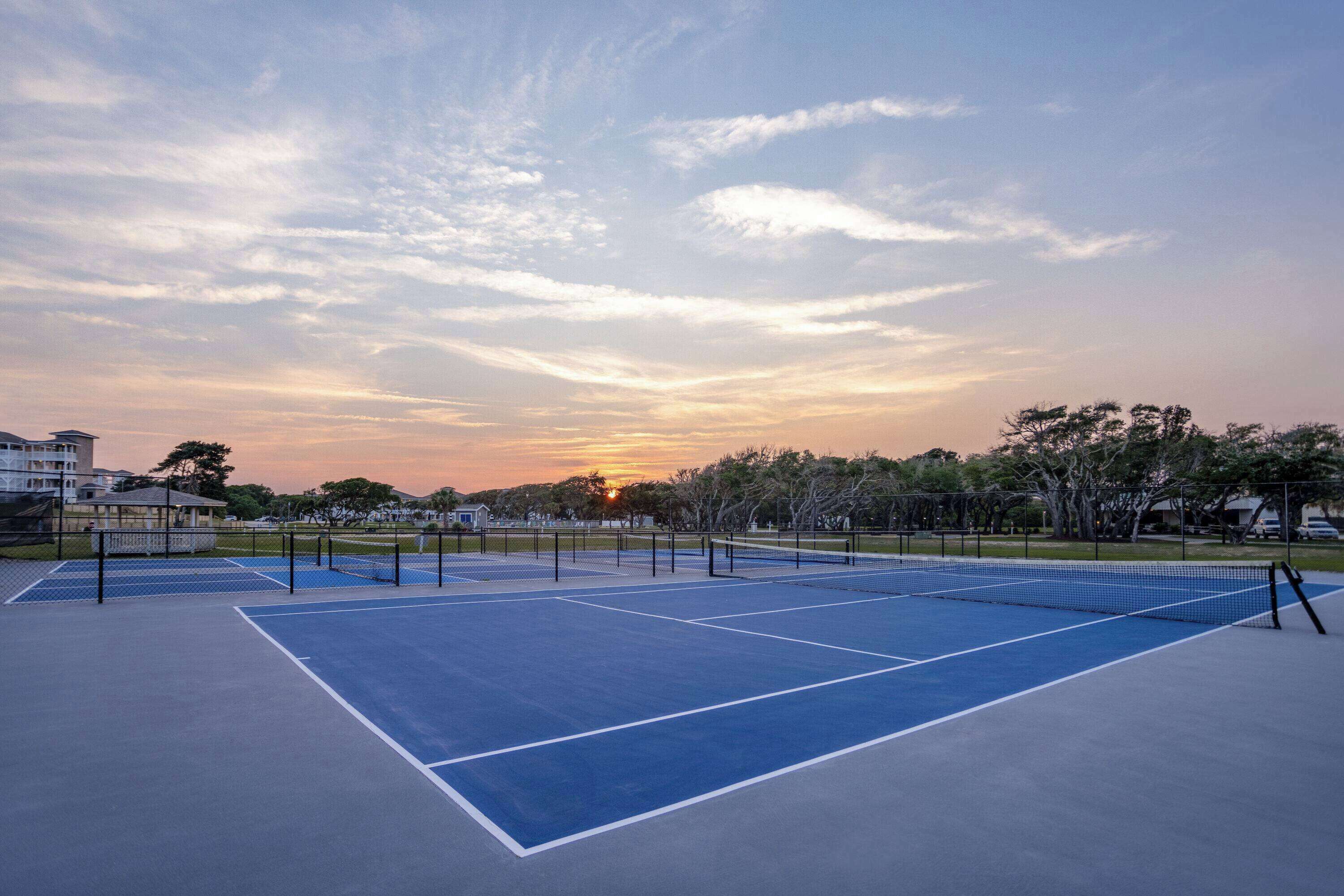 An outdoor tennis court with a sunset in the background.
