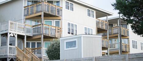 A multi-story residential building with balconies, wooden railings, and a small utility shed.