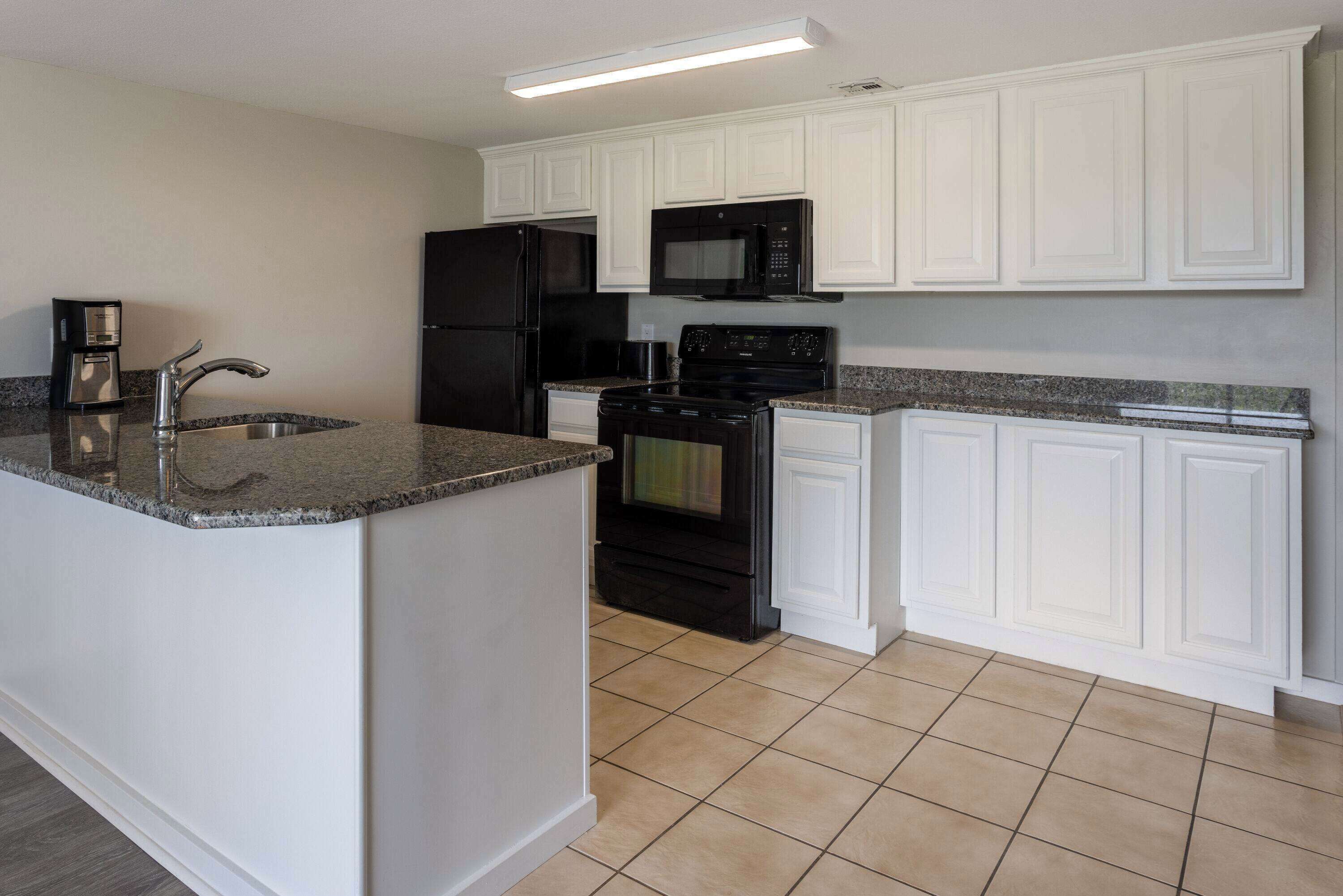 A kitchen with white cabinets, a black refrigerator, a microwave, a stove, and a granite countertop.
