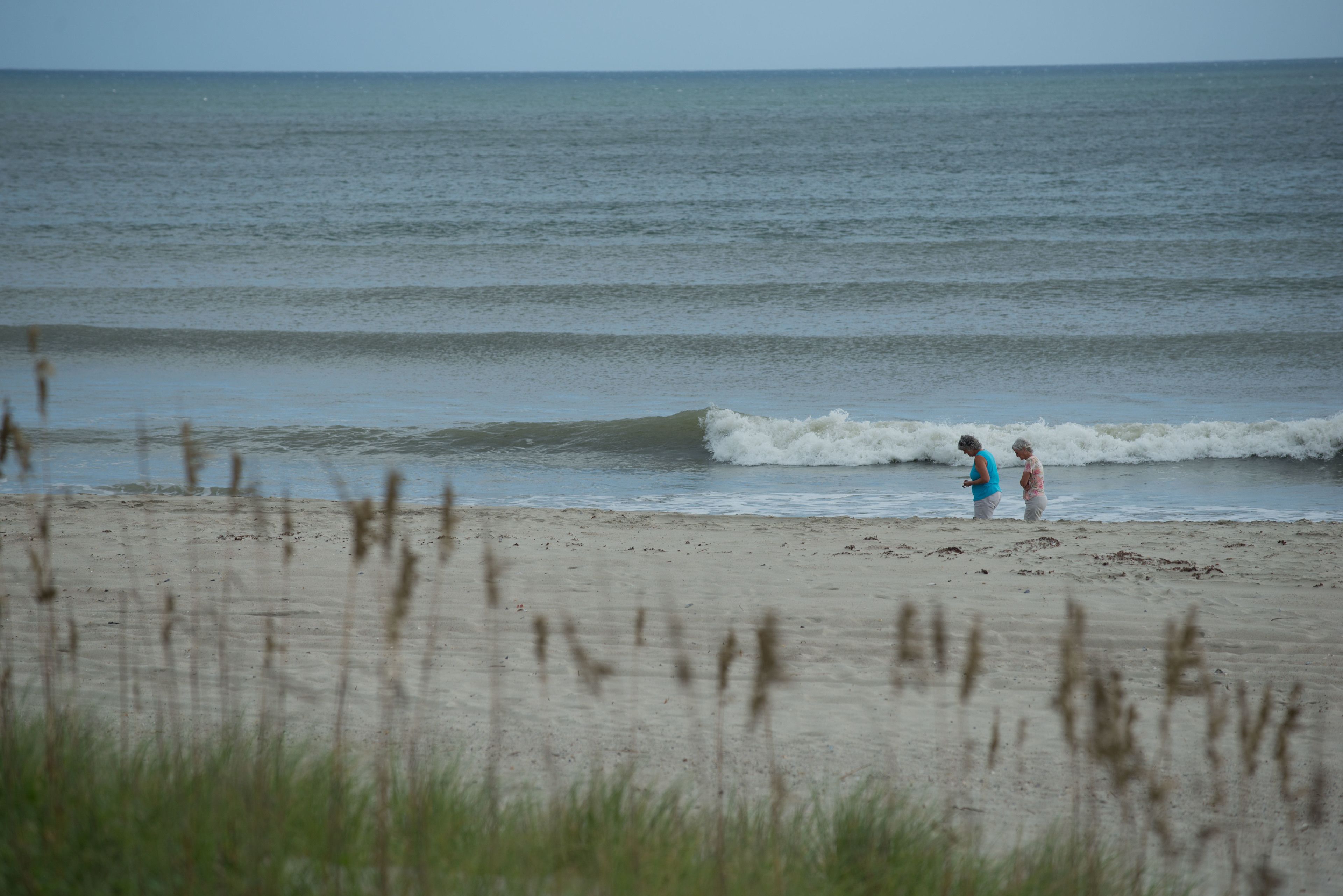 A beach with two people standing near the water's edge.