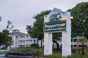 Peppertree Atlantic Beach Villas -hotellin opastekyltti, jossa näkyy useita kerroksia sisältävä rakennus, jossa on parvekkeita, sekä hyvin hoidettu puutarha-alue.