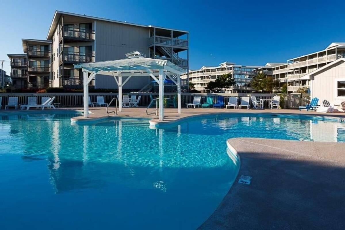 A swimming pool with lounge chairs and a covered area, surrounded by multi-story buildings.