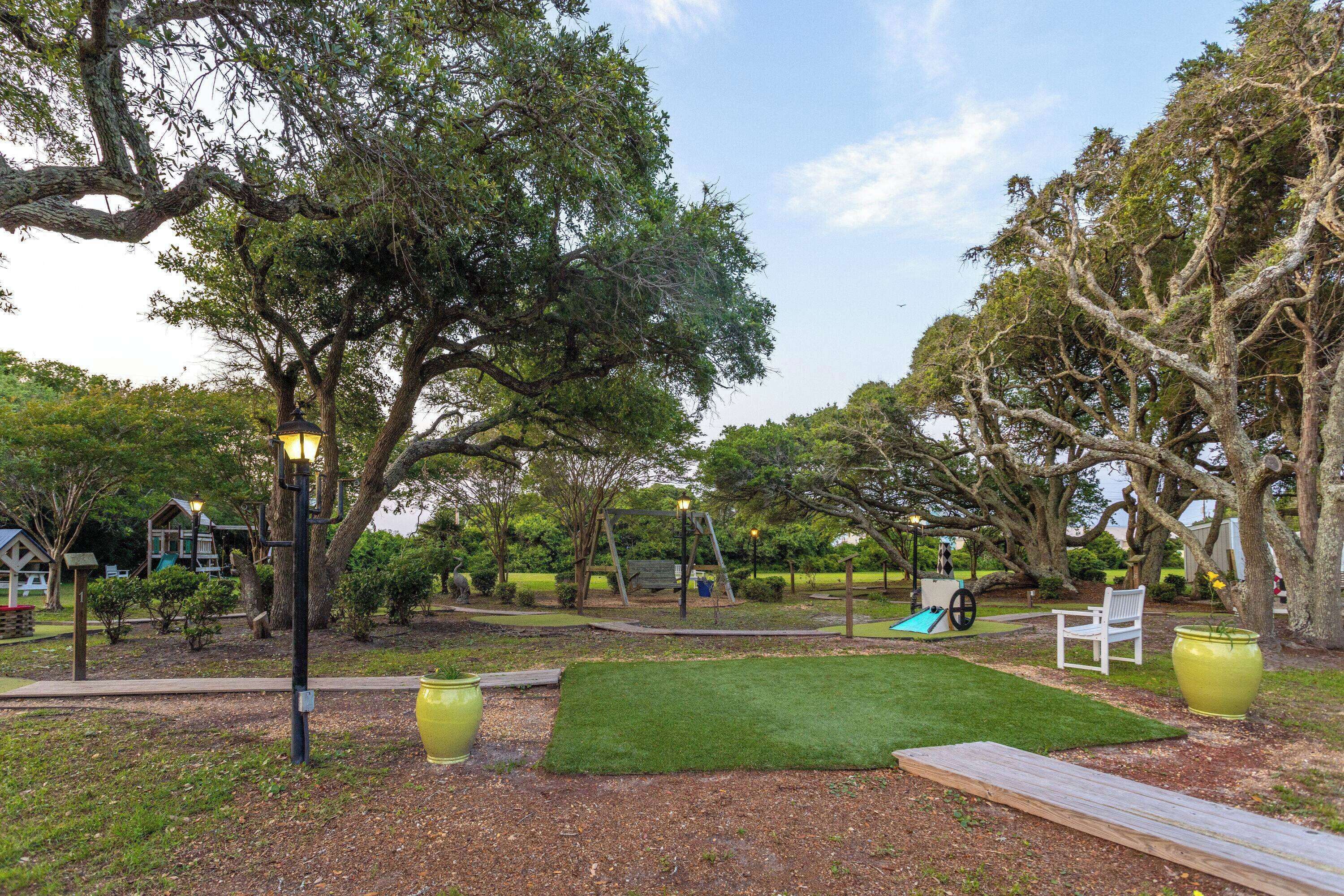 A park with a wooden deck, a green lawn, and a swing set.