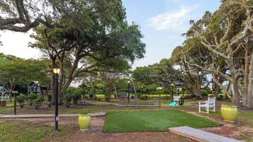 A park with a wooden deck, a green lawn, and a swing set.