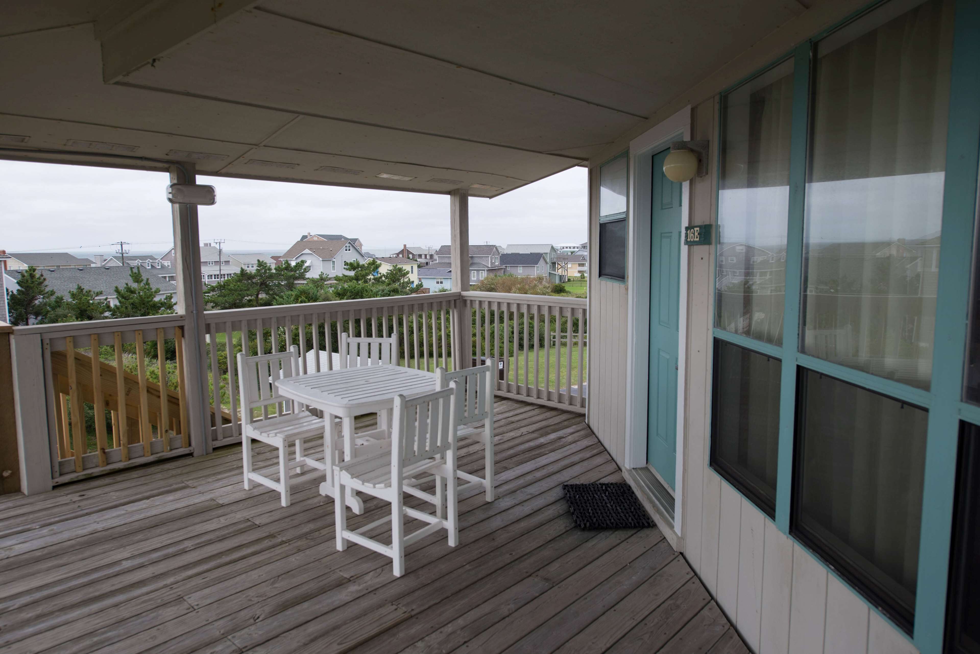 A covered outdoor area with a wooden deck, a white table and chairs, and a view of houses in the distance.