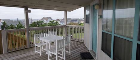 A covered outdoor area with a wooden deck, a white table and chairs, and a view of houses in the distance.