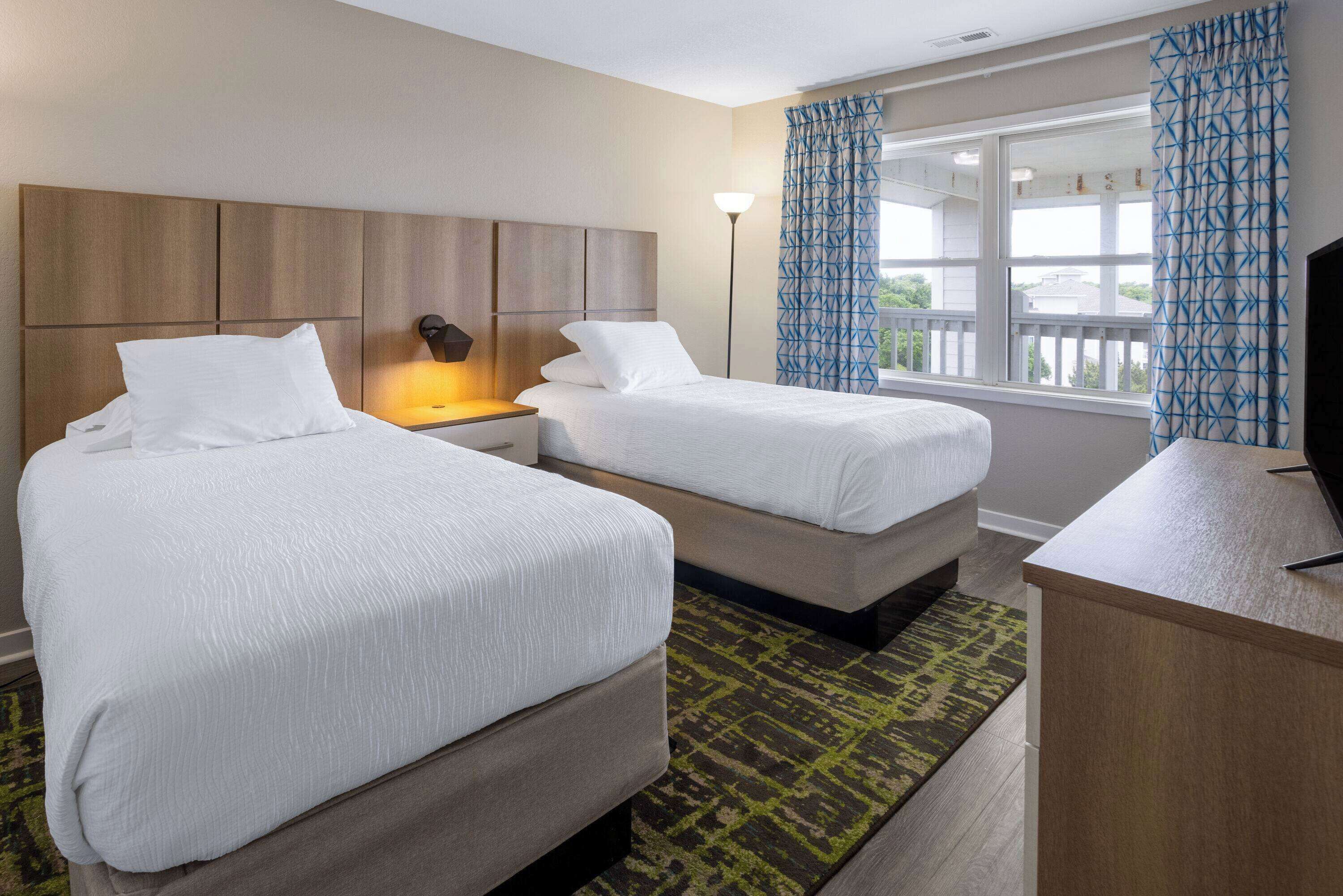 Une chambre d’hôtel avec deux lits, un bureau, une lampe et une vue sur l’extérieur.