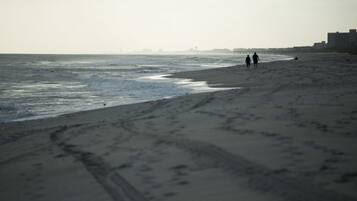 A beach with footprints leading to the water, a distant pier, and buildings in the background.