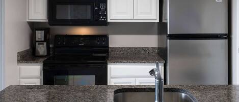 A kitchen with white cabinets, a black microwave, a stainless steel refrigerator, a black stove, and a granite countertop.