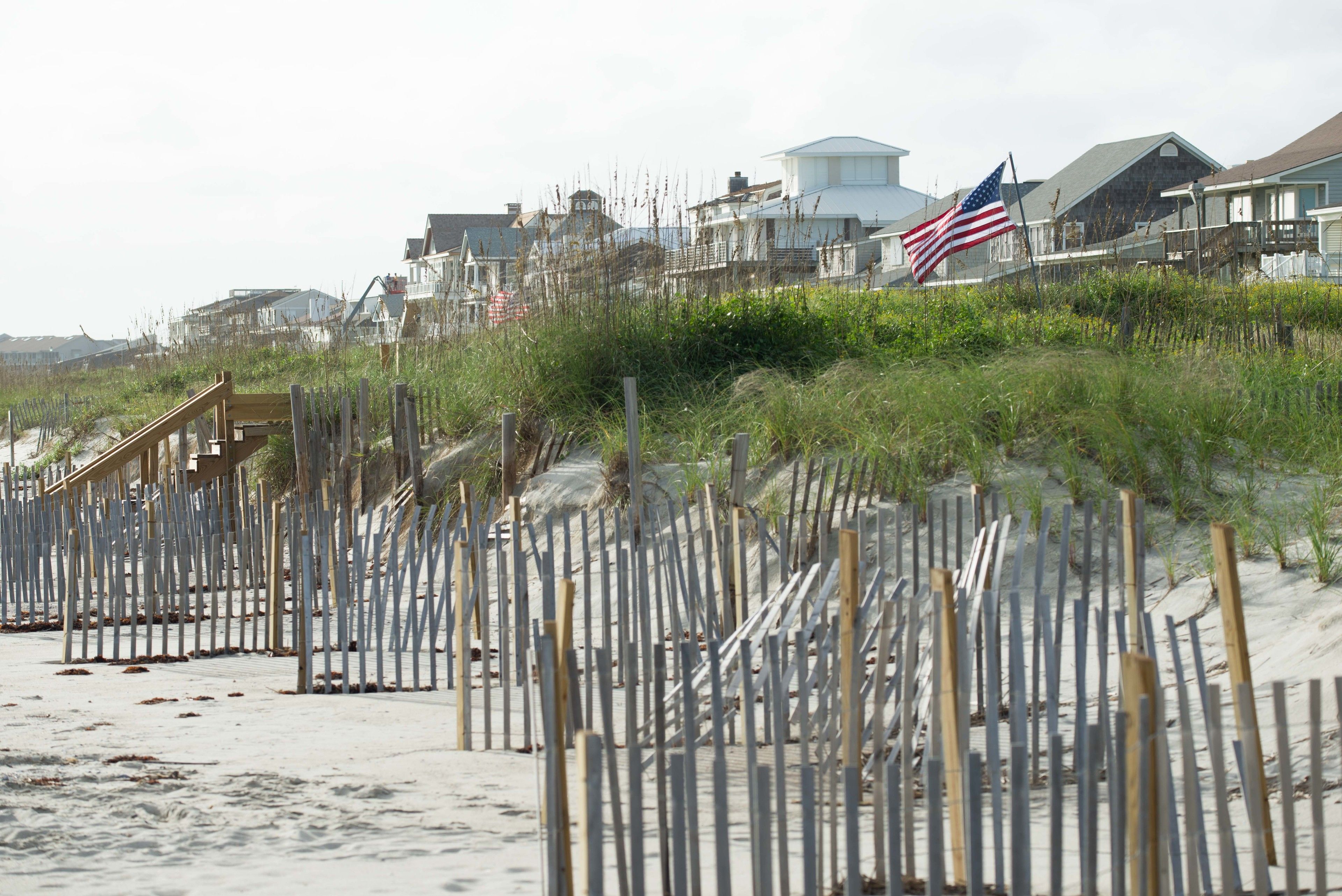 A beach with wooden barriers, a wooden staircase, and houses in the background.