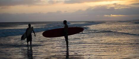 Two people walking on a beach with surfboards, under a sunset sky.