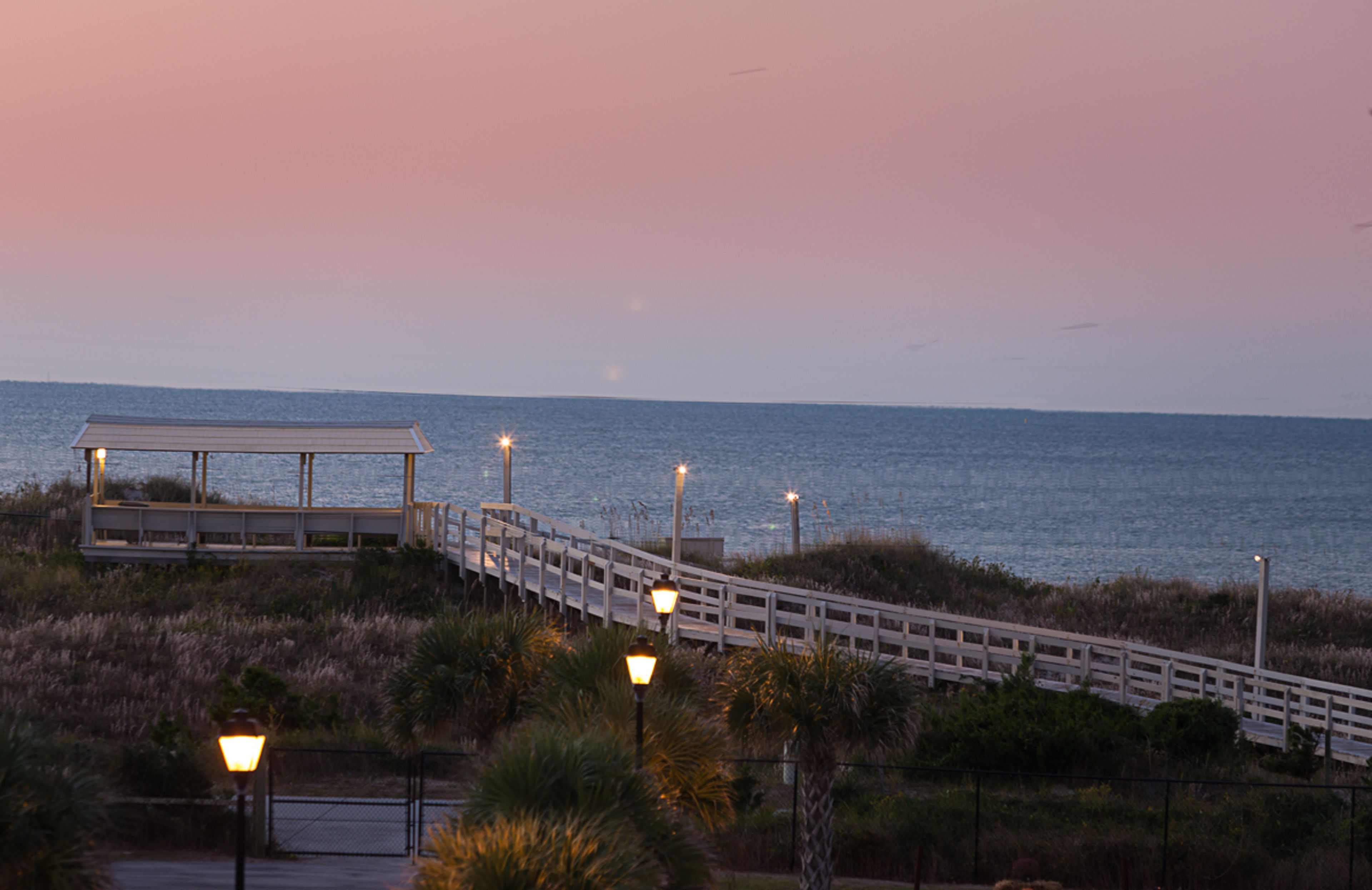 A boardwalk leading to a gazebo by the water at dusk.