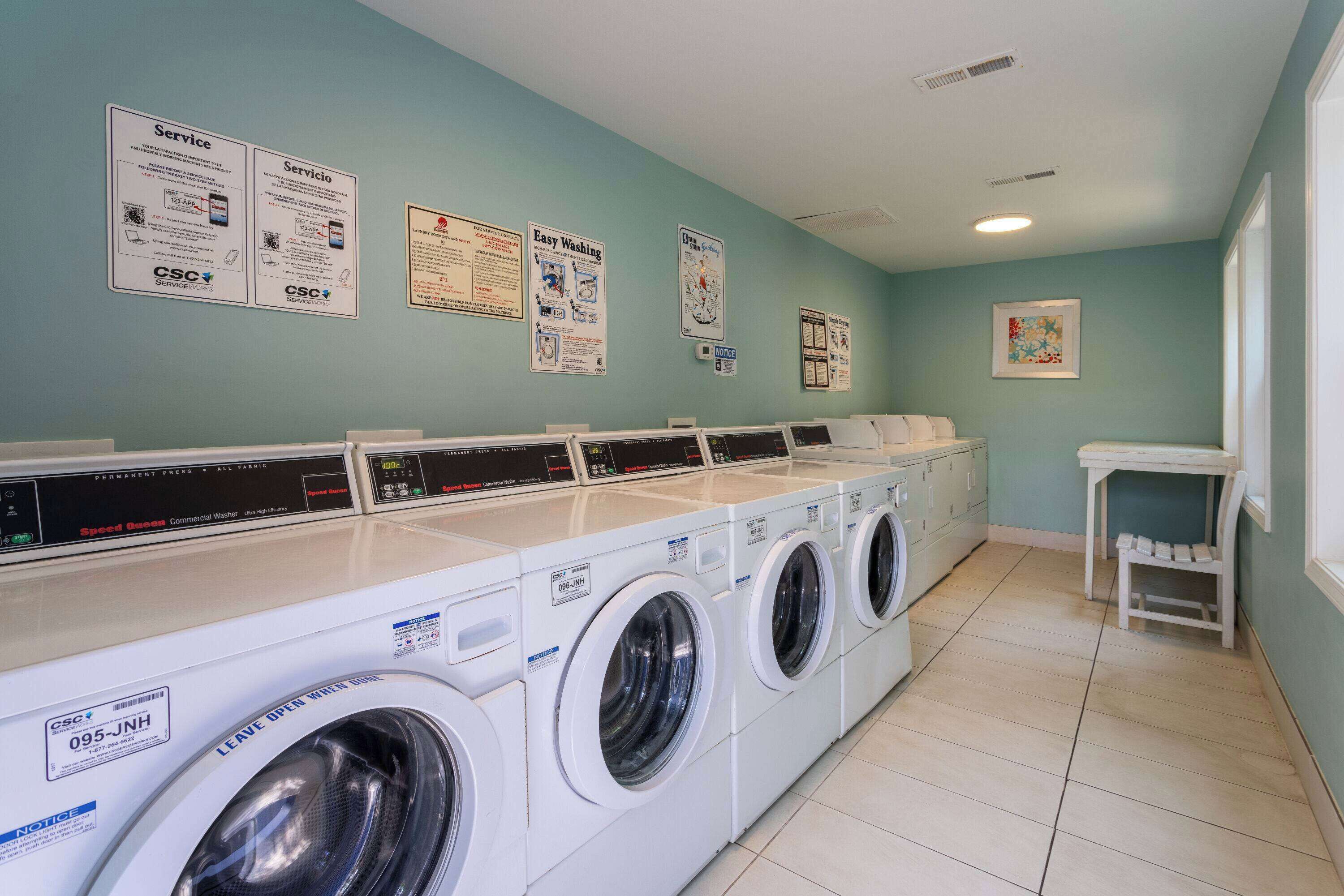 A laundry facility with multiple washing machines, instructional posters on the wall, and a small table with a chair.