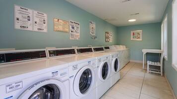 A laundry facility with multiple washing machines, instructional posters on the wall, and a small table with a chair.