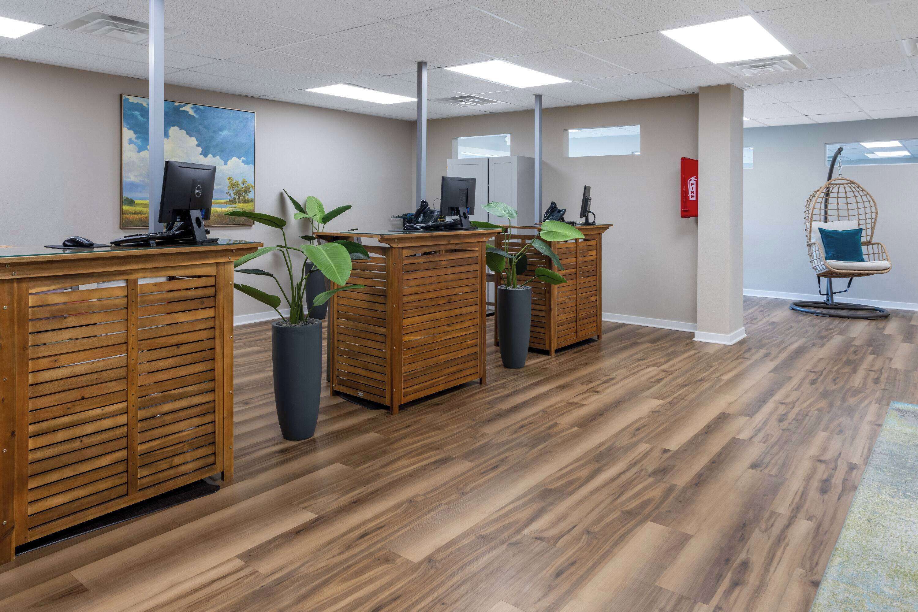 A reception area with wooden desks, potted plants, a hanging chair, and a painting on the wall.