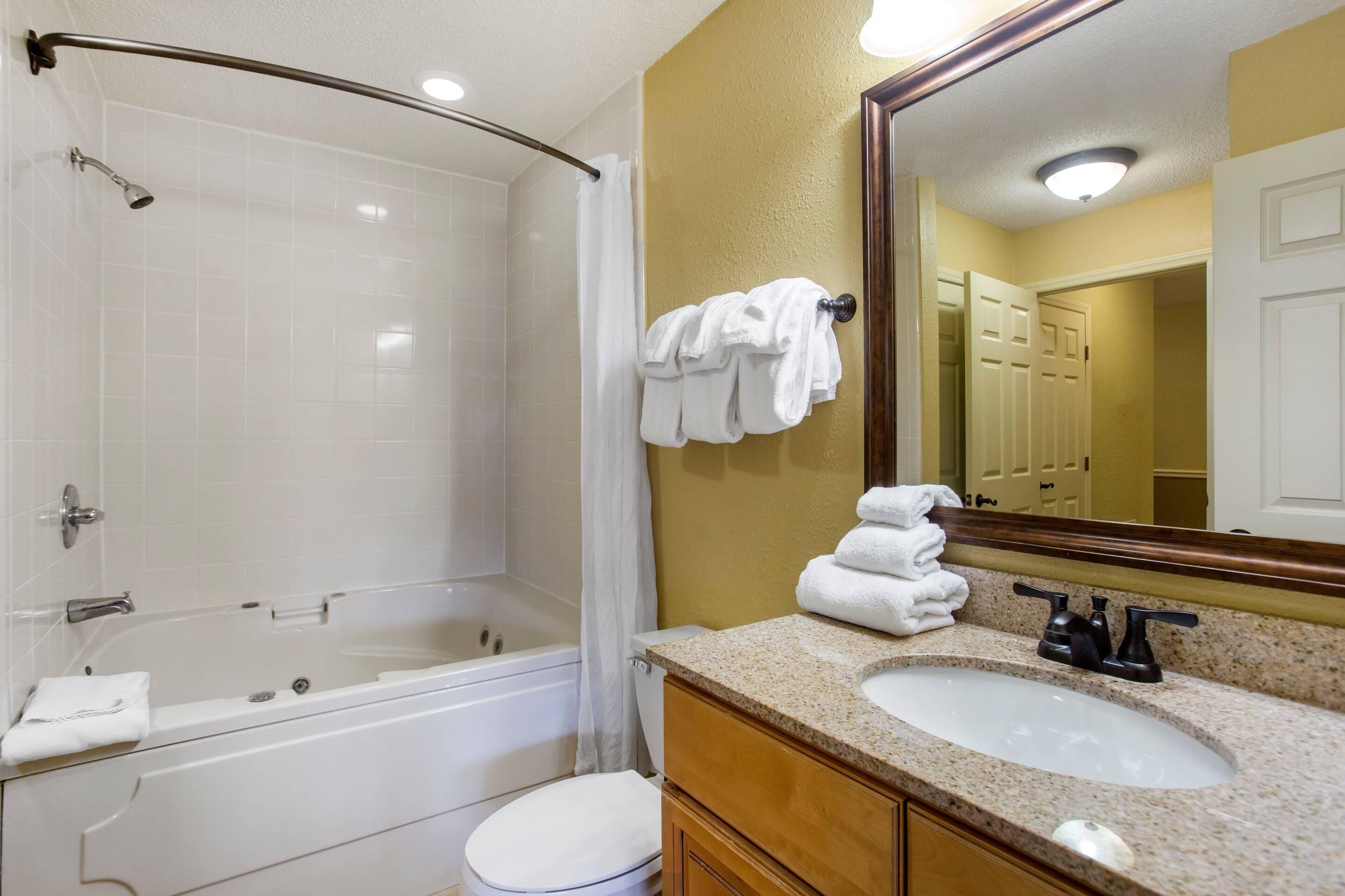 Un baño con bañera, inodoro, lavamanos y espejo.
