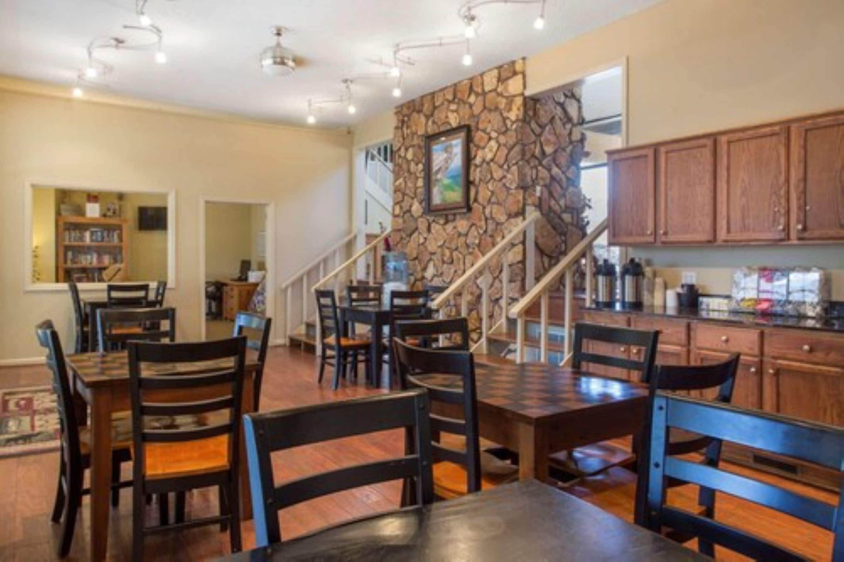 Un espace repas avec des tables et des chaises en bois, un mur décoratif en pierre et un escalier menant à un autre niveau.