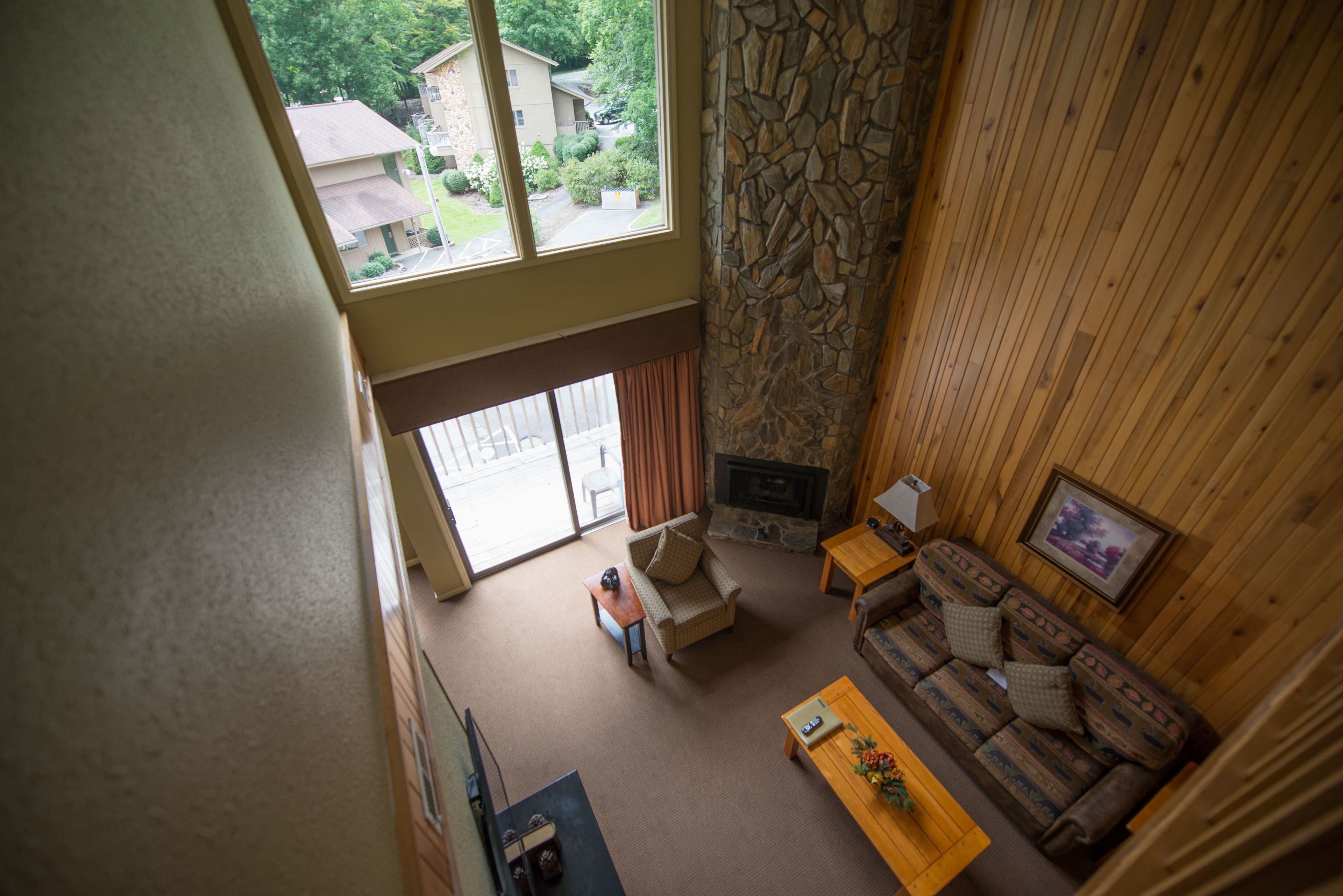 A spacious living room with a stone fireplace, a wooden sofa, and a view of the outside.