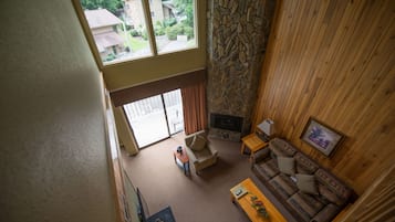 Un salón amplio con chimenea de piedra, un sofá de madera y vistas al exterior.