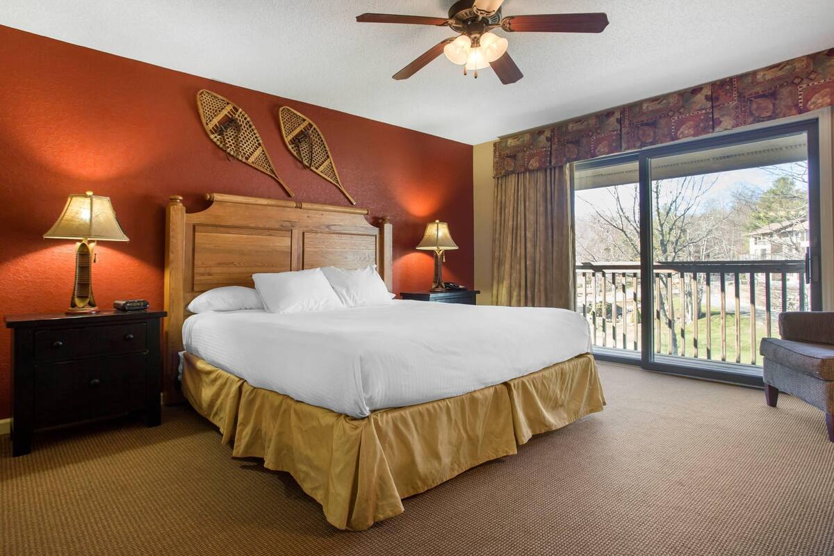 A hotel room with a large bed, two bedside tables with lamps, a ceiling fan, and a balcony with a view.