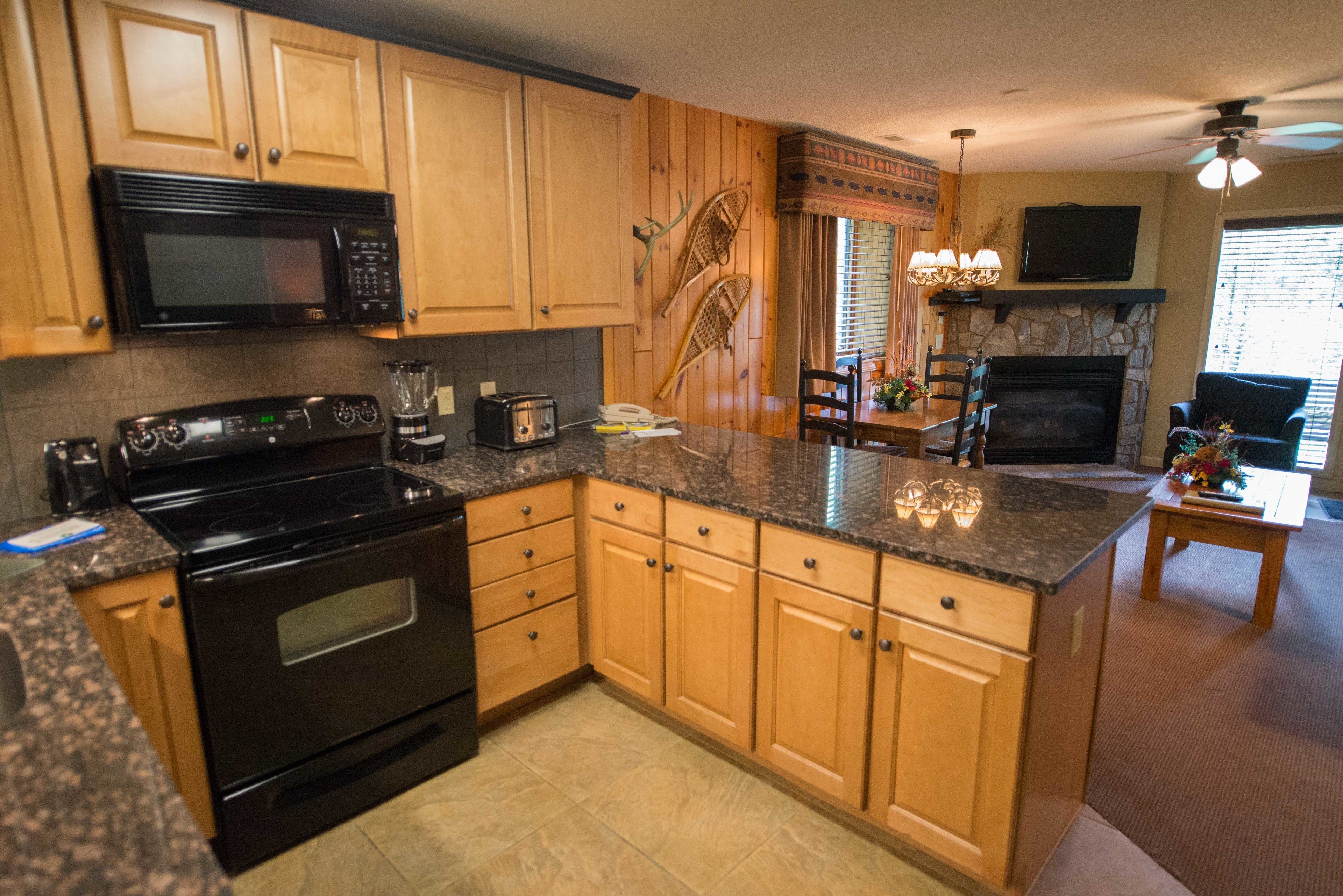 A kitchen with wooden cabinets, a black stove, a microwave, and a stone fireplace.