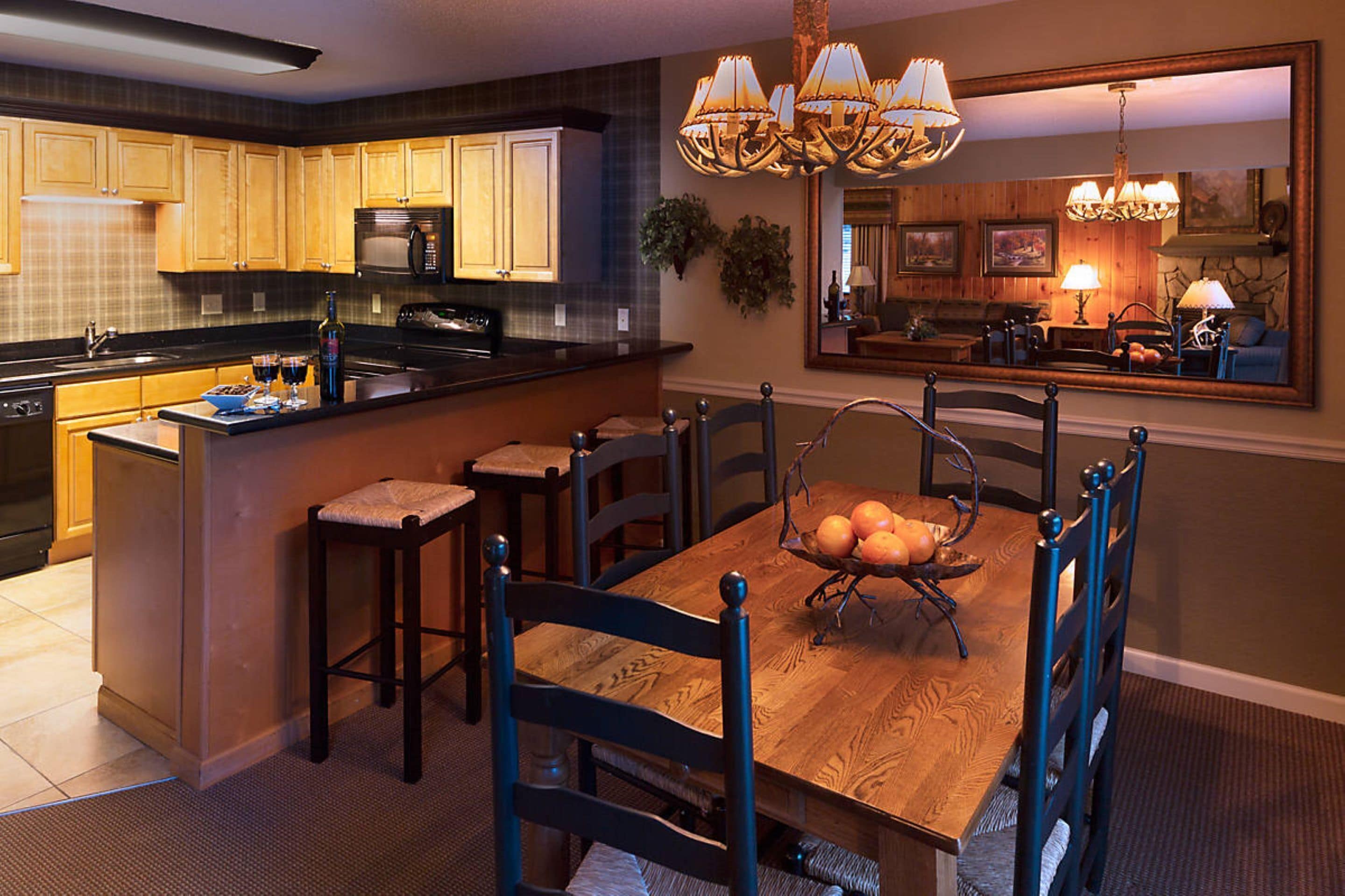 A kitchen with wooden cabinets, a central island with stools, a dining table with chairs, and a chandelier.