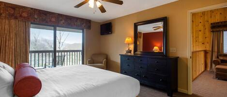A hotel room with a bed, a ceiling fan, a dresser, a chair, a television, and a view of the outdoors.