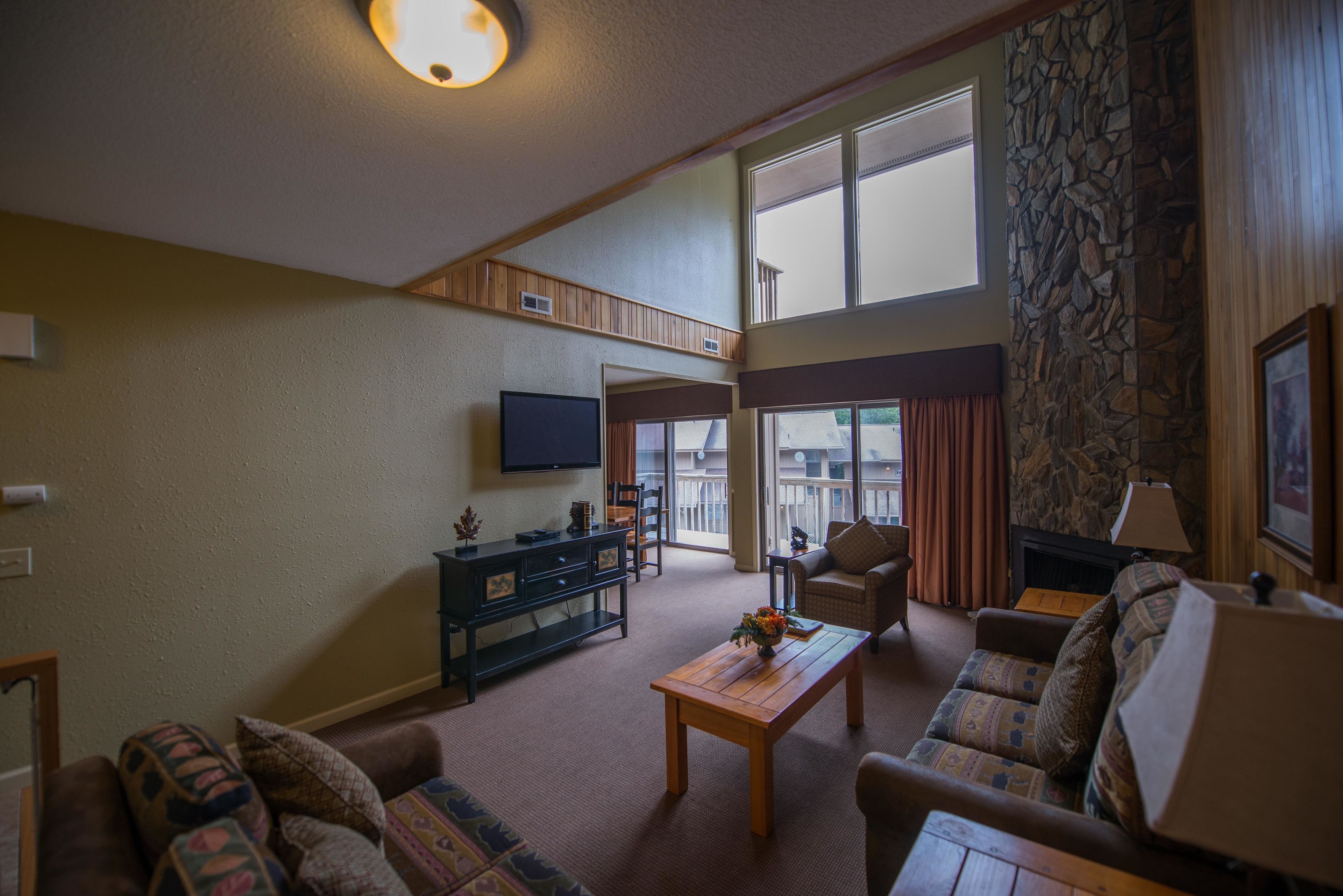 Een ruime woonkamer met een hoge plafond, een stenen openhaard en een aan de muur bevestigde televisie.