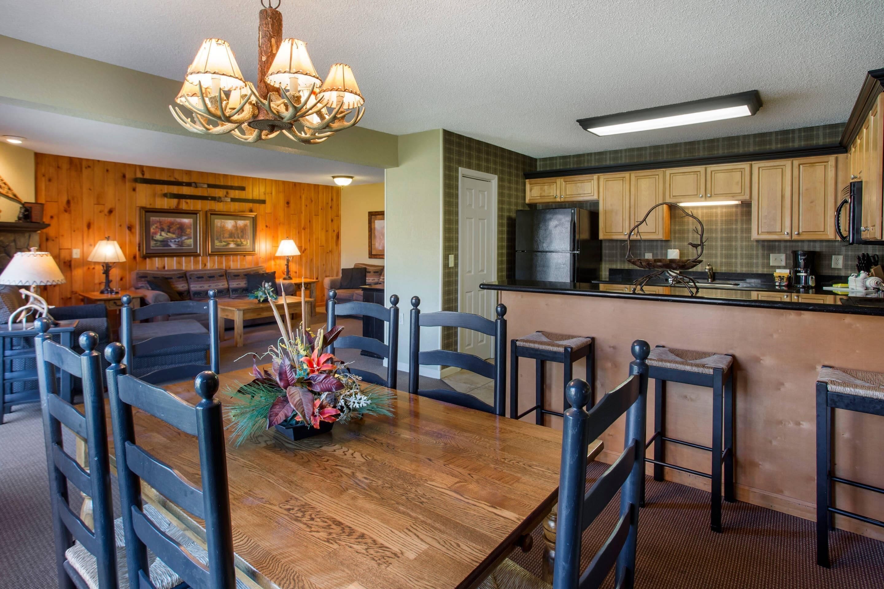 A dining area with a wooden table and chairs, a chandelier, and a kitchen with wooden cabinets and appliances.