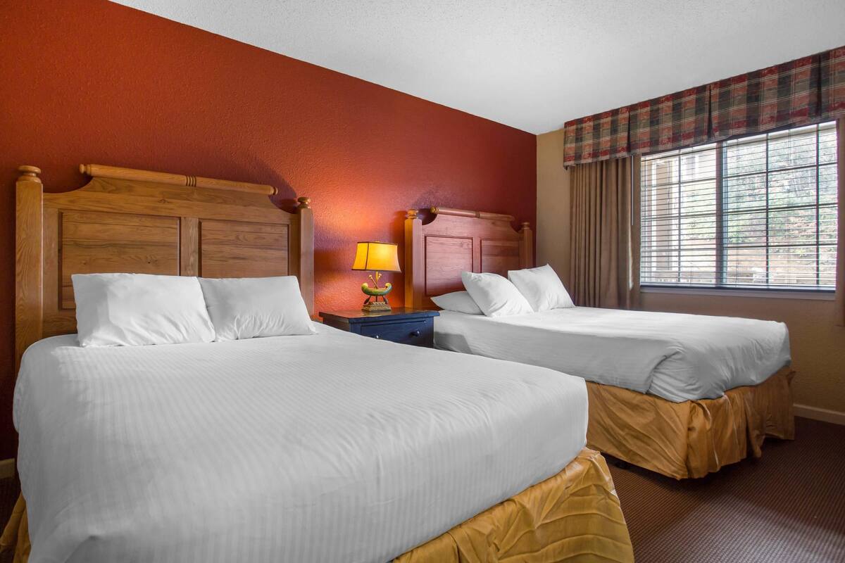 A hotel room with two beds, a nightstand with a lamp, and a window with curtains.