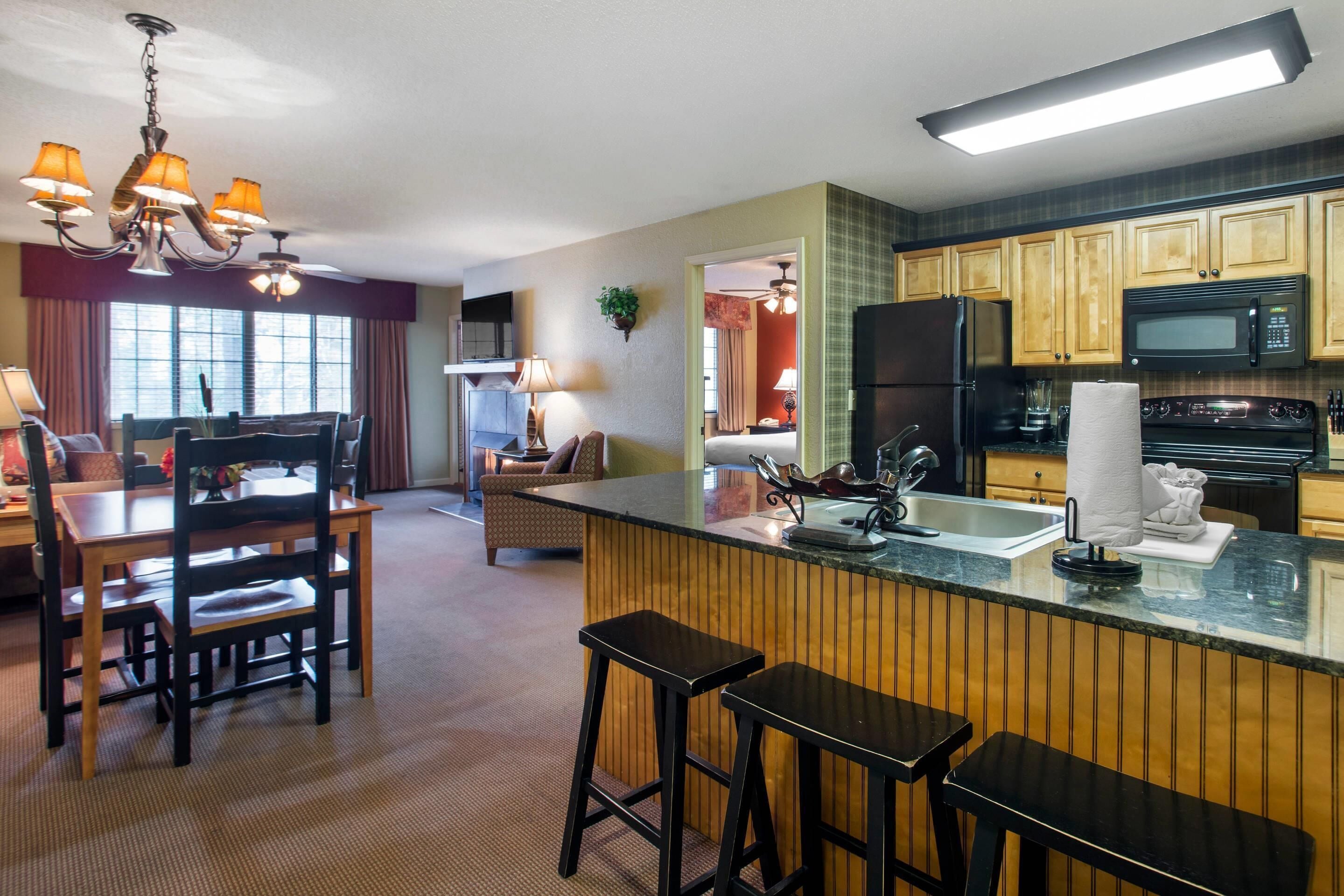 A modern kitchen with wooden cabinets, a black refrigerator, a microwave, and a bar area with stools.
