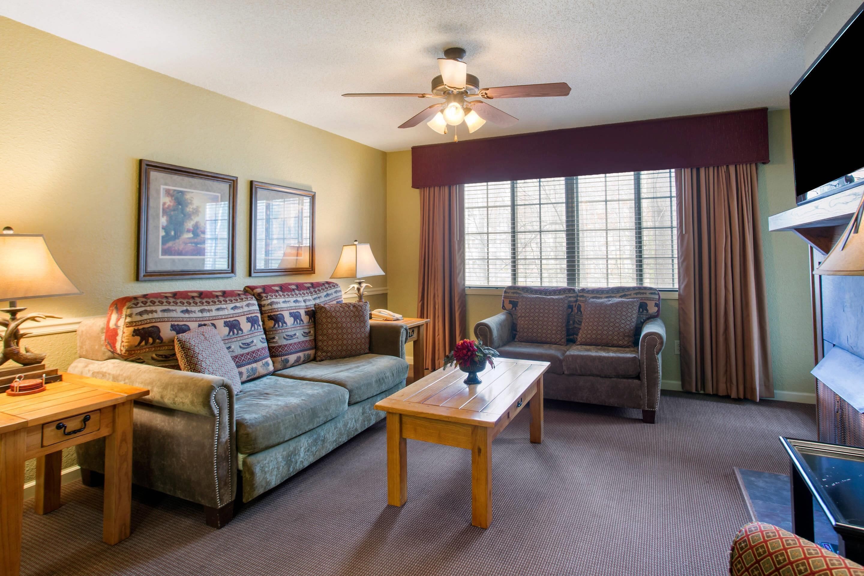 A living room with a sofa, armchair, wooden coffee table, and a ceiling fan.