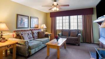 A living room with a sofa, armchair, wooden coffee table, and a ceiling fan.