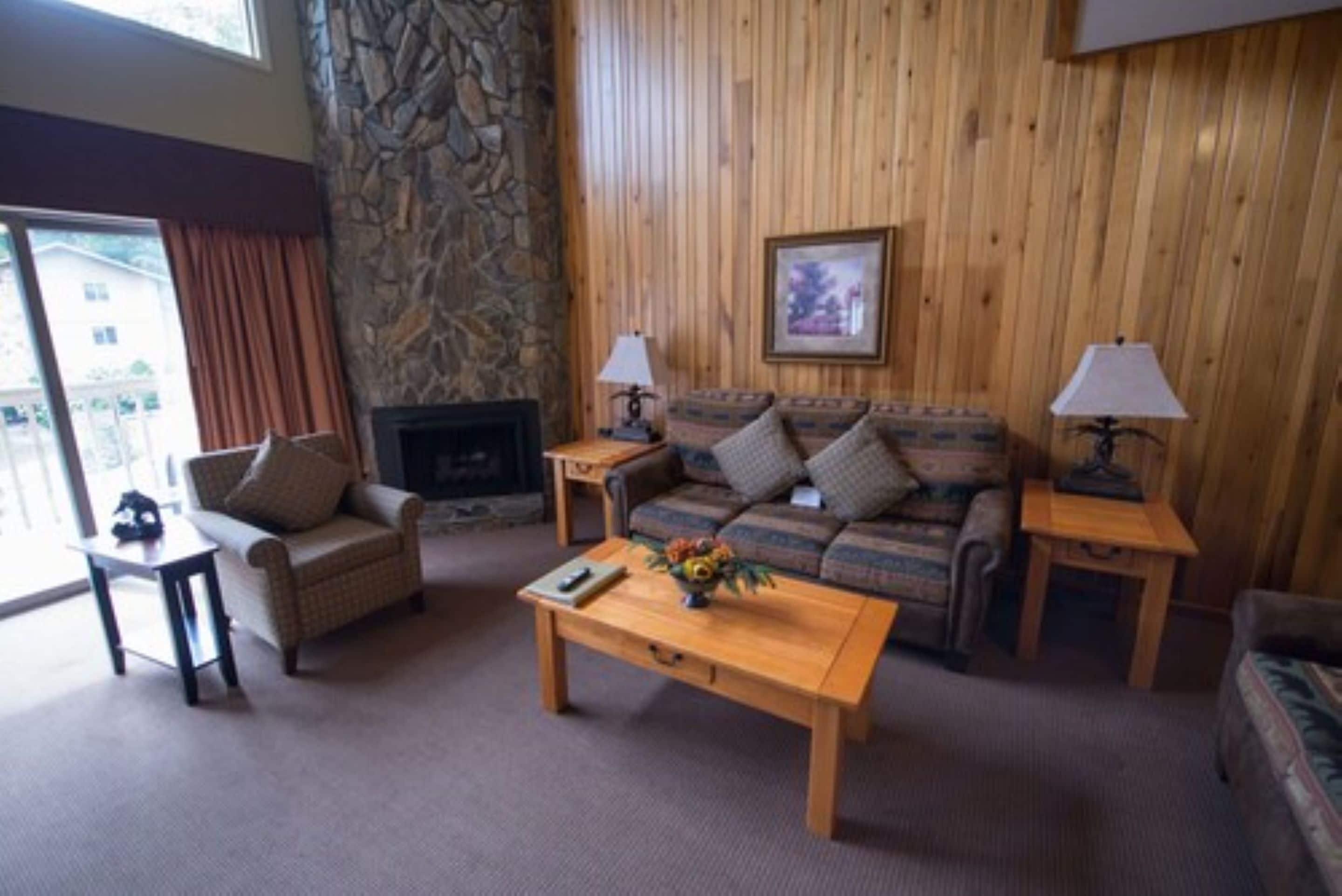 Una sala de estar acogedora con una pared de acento de piedra, una chimenea, un conjunto de sofá y una mesa de centro.