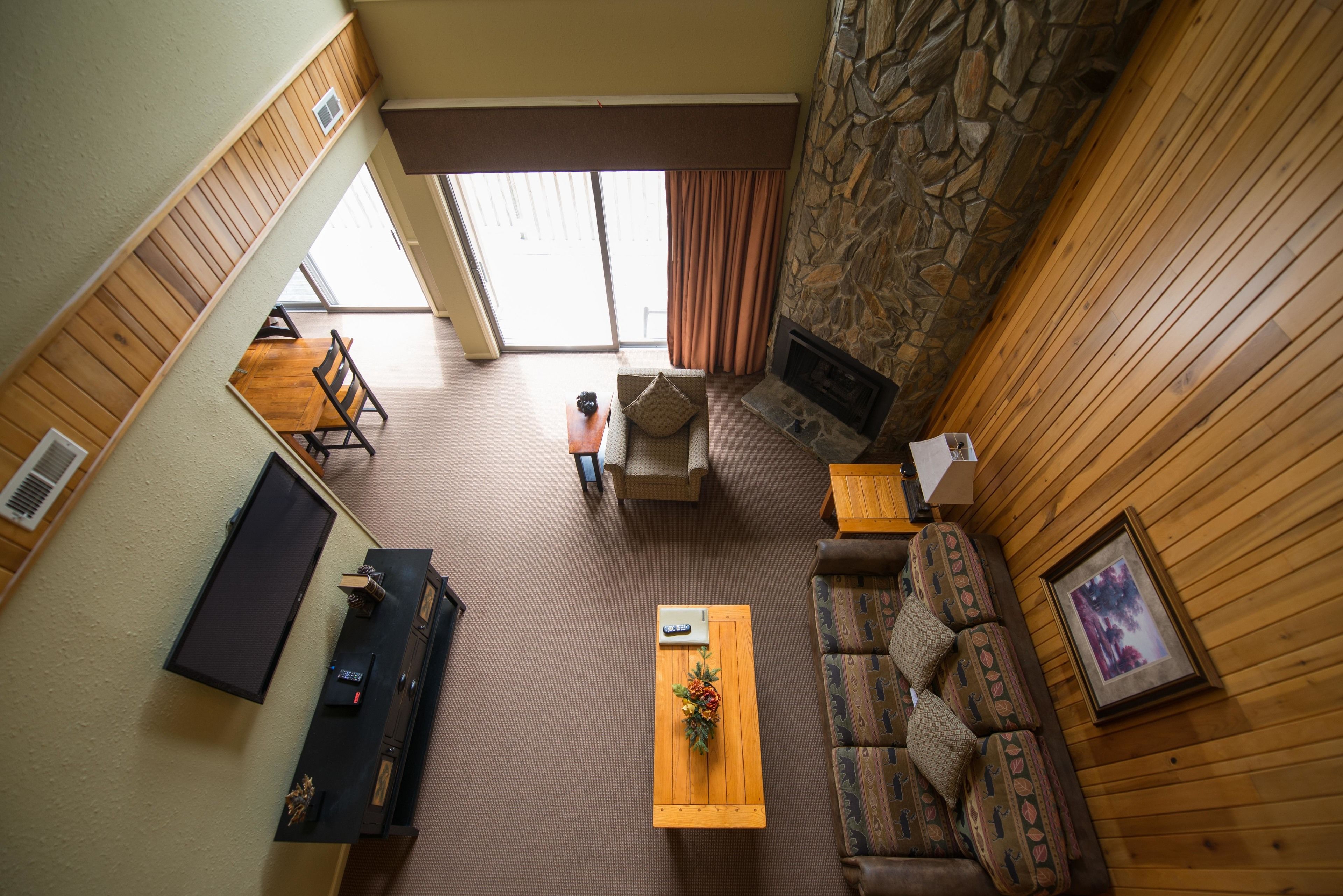 A spacious living area with a stone fireplace, wooden walls, a sofa, a coffee table, and a TV.