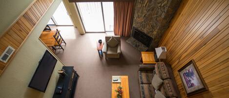 A spacious living area with a stone fireplace, wooden walls, a sofa, a coffee table, and a TV.