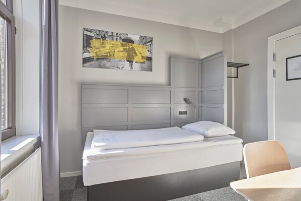 A hotel room with a bed, a window, a wall-mounted artwork, and a door.