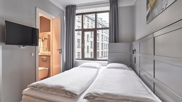 A hotel room with a bed, a TV, a window with curtains, and a view of buildings outside. - Four Points Flex by Sheraton Copenhagen City (Copenhagen)