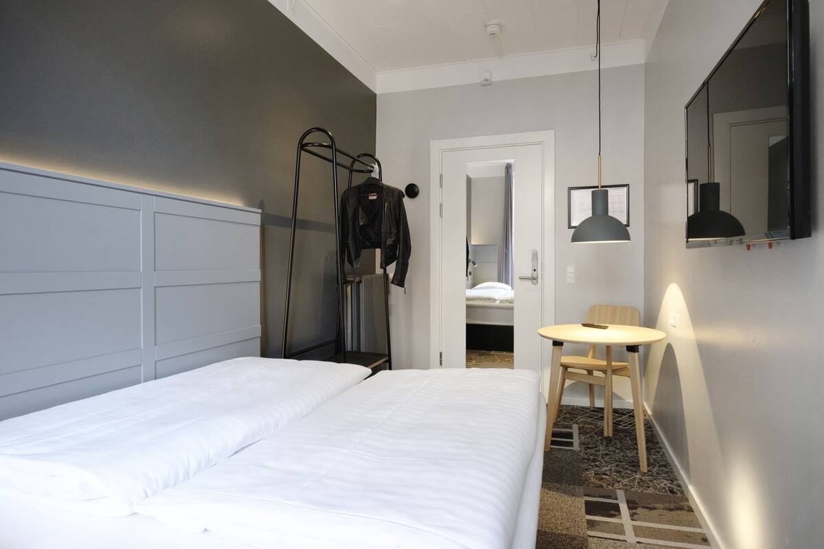 Una camera d'albergo con un letto grande, un tavolino, una sedia, uno specchio e un termosifone.