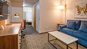 Habitación de hotel con un escritorio de madera, un sofá azul, una mesita pequeña y un suelo estampado.