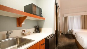 Habitación de hotel compacta con kitchenette, que incluye un lavamanos, microondas y refrigerador.