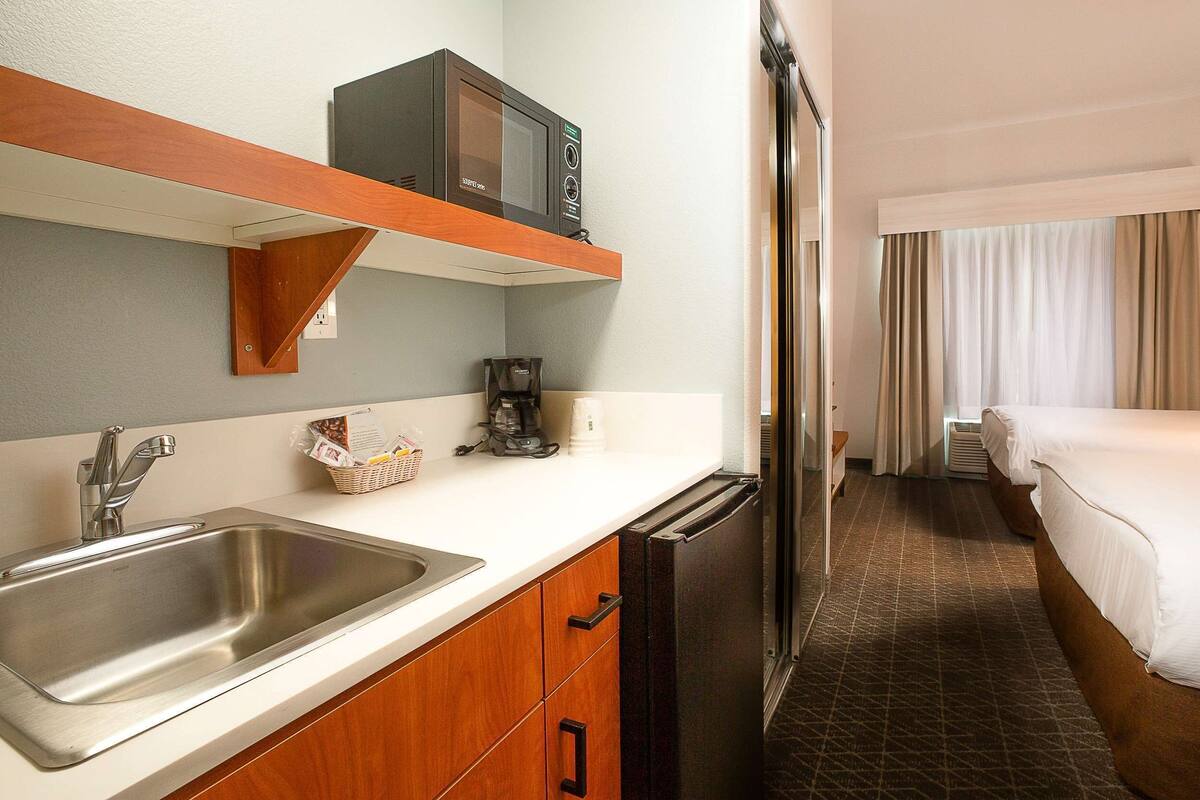 A compact hotel room with a kitchenette, including a sink, microwave, and refrigerator.