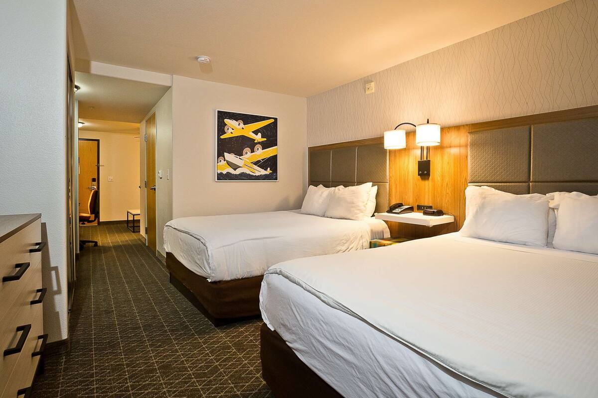 A hotel room with two beds, a headboard, bedside lamps, a telephone, and a painting on the wall.