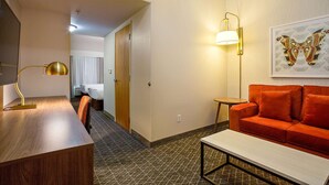 Habitación de hotel con un escritorio de madera, un sofá rojo, una mesa de centro blanca, una lámpara de pared y una obra de arte con una mariposa enmarcada.