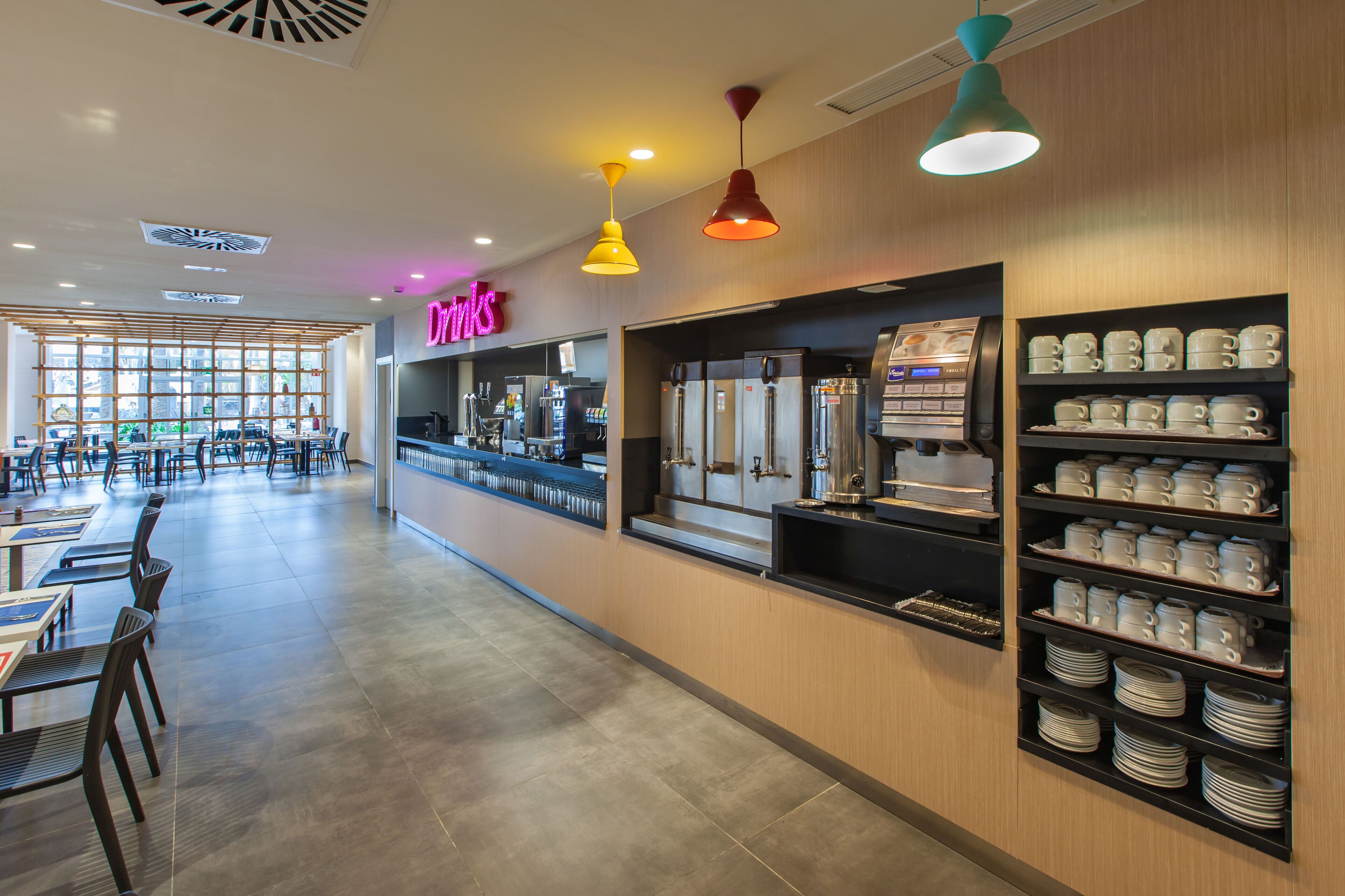 Un café moderno con barra, zona de mesas y exhibición de tazas y platillos.